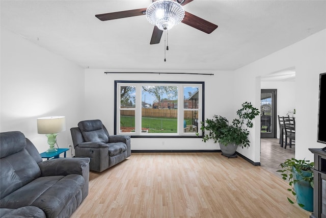living room featuring baseboards, ceiling fan, light wood-style floors, and plenty of natural light