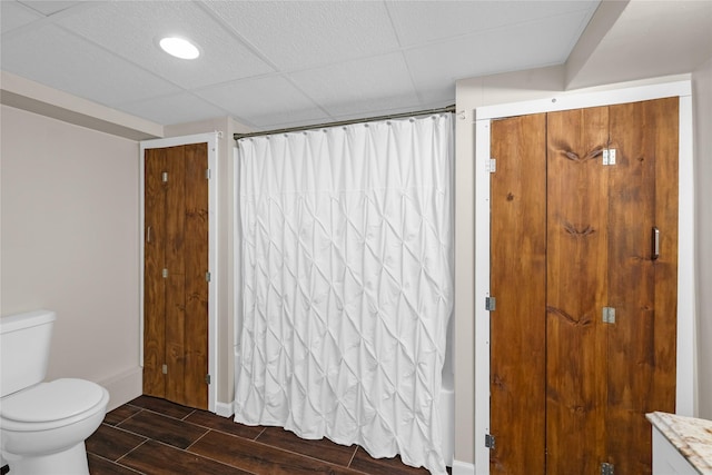 full bathroom with a drop ceiling, a shower with curtain, toilet, baseboards, and wood tiled floor