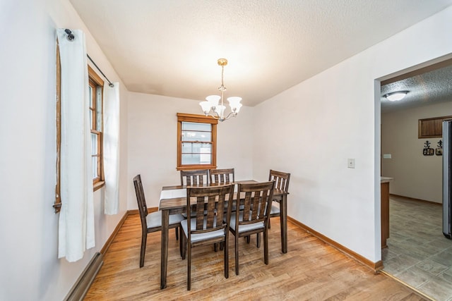 dining space with a baseboard heating unit, light wood finished floors, an inviting chandelier, baseboards, and a textured ceiling