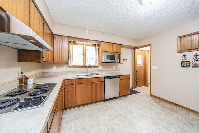 kitchen with a sink, brown cabinetry, ventilation hood, light countertops, and appliances with stainless steel finishes