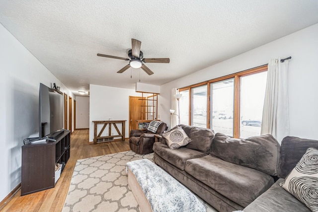 living area featuring baseboards, a ceiling fan, a textured ceiling, and light wood finished floors
