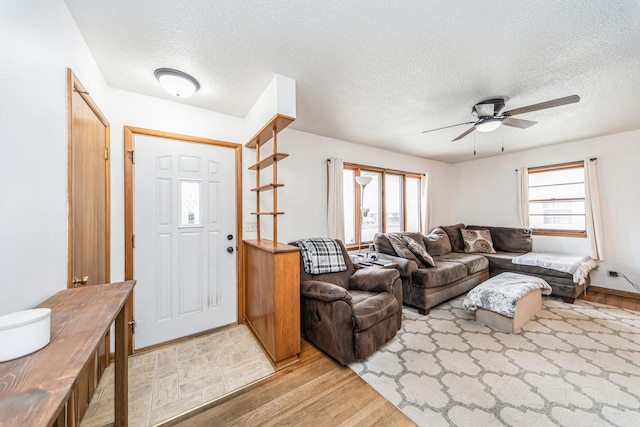 living room with a ceiling fan, a textured ceiling, and light wood-style flooring