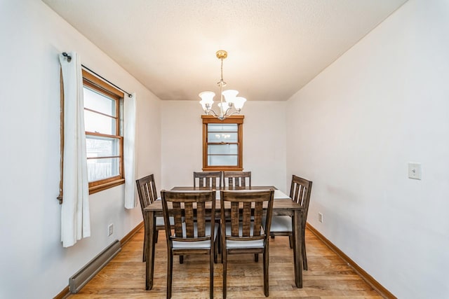 dining space featuring an inviting chandelier, a baseboard radiator, light wood-type flooring, and baseboards