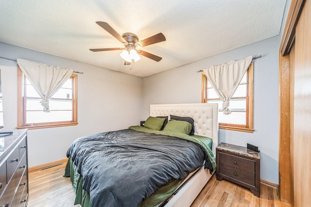 bedroom featuring light wood finished floors, a ceiling fan, visible vents, baseboards, and a textured ceiling