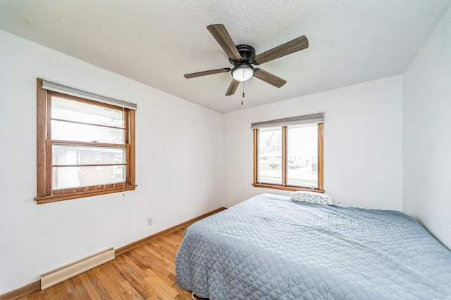 bedroom with baseboards, multiple windows, light wood finished floors, and a baseboard radiator