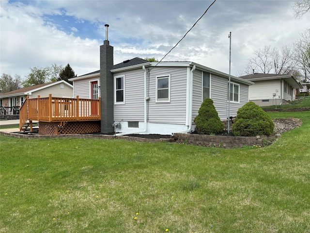 back of property with a chimney, a wooden deck, and a yard