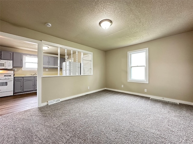spare room featuring visible vents, dark carpet, a healthy amount of sunlight, and baseboards