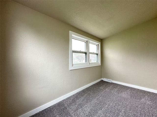 empty room featuring dark colored carpet, visible vents, and baseboards