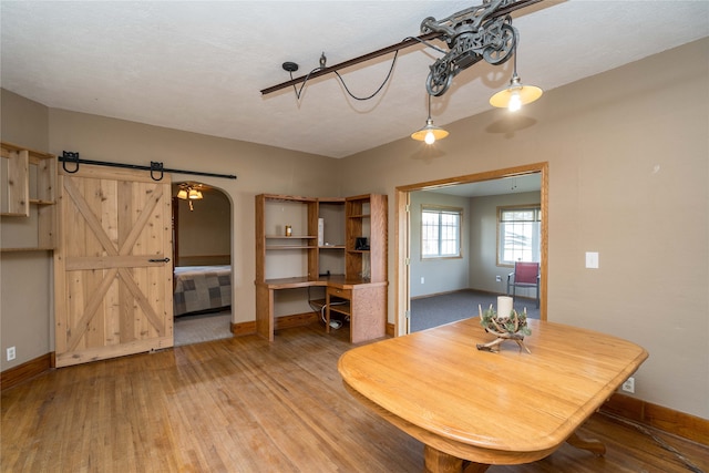 dining area featuring baseboards, light wood-type flooring, arched walkways, and a barn door