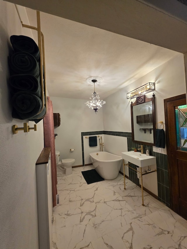 full bath featuring a notable chandelier, a freestanding tub, toilet, marble finish floor, and baseboards