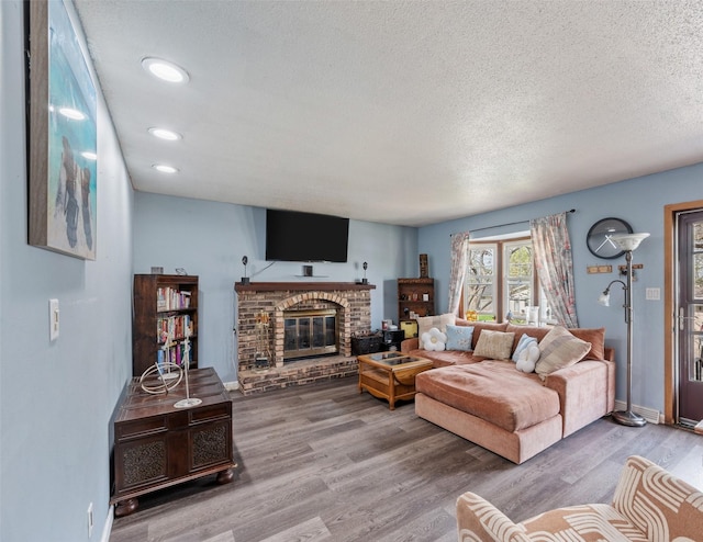 living room with a textured ceiling, baseboards, recessed lighting, a fireplace, and wood finished floors