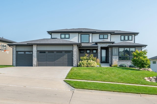 prairie-style house featuring driveway, a front lawn, an attached garage, and stone siding