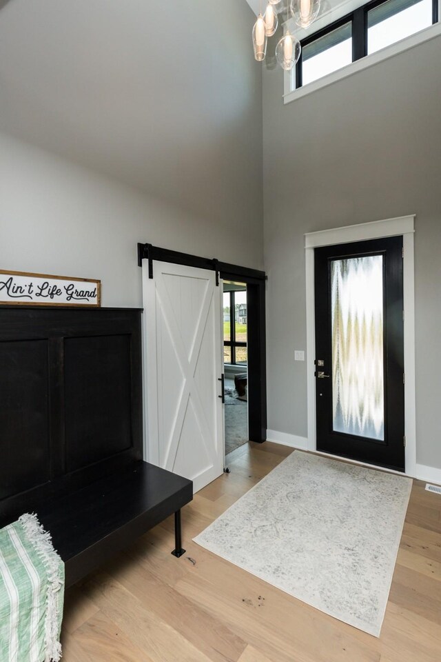foyer entrance featuring light wood-style flooring, a barn door, baseboards, an inviting chandelier, and a high ceiling