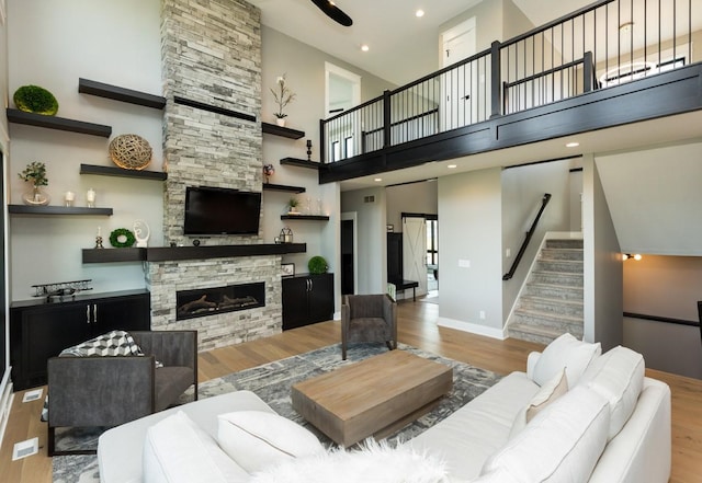 living area with a towering ceiling, stairs, a stone fireplace, and wood finished floors