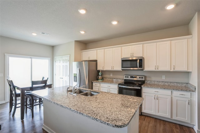kitchen featuring white cabinets, appliances with stainless steel finishes, visible vents, dark wood-style floors, and a kitchen island with sink