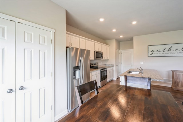 kitchen with white cabinets, a sink, stainless steel appliances, baseboards, and a center island with sink