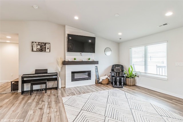 living area featuring visible vents, baseboards, a glass covered fireplace, vaulted ceiling, and wood finished floors