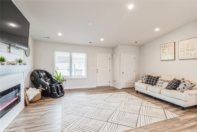 living room with visible vents, baseboards, a glass covered fireplace, light wood-type flooring, and recessed lighting