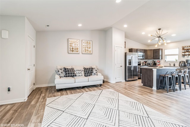 living room with an inviting chandelier, light wood-style flooring, lofted ceiling, and baseboards