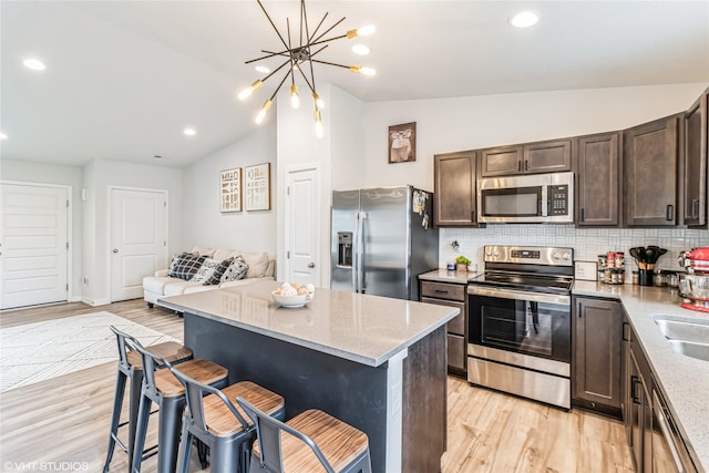 kitchen with light wood finished floors, appliances with stainless steel finishes, decorative backsplash, vaulted ceiling, and dark brown cabinets