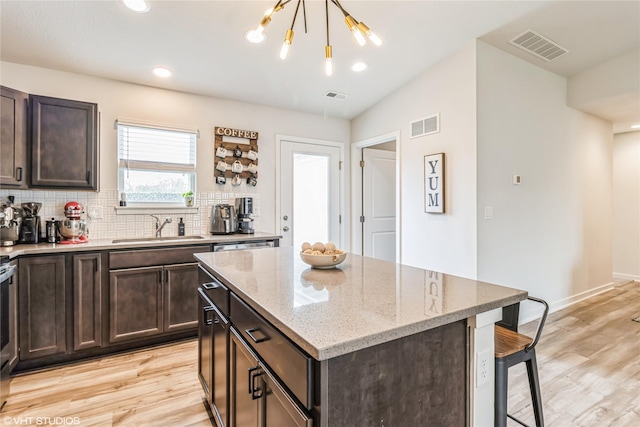kitchen featuring light wood-style floors, backsplash, a sink, visible vents, and a kitchen breakfast bar