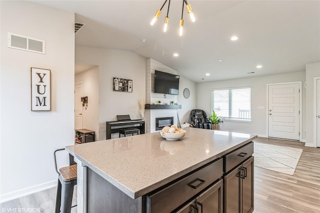 kitchen with a fireplace, visible vents, light stone counters, and light wood finished floors