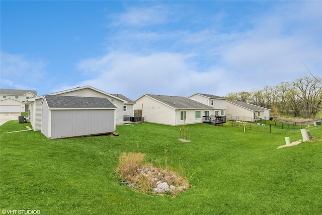 rear view of property with an outdoor structure, a yard, a storage unit, and fence