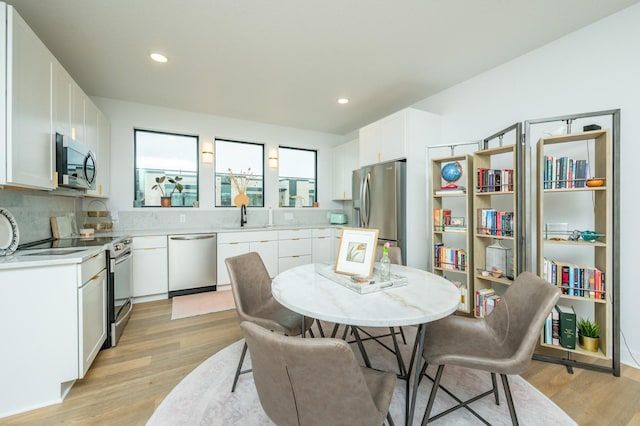 kitchen with white cabinets, a sink, light countertops, light wood-style flooring, and stainless steel appliances