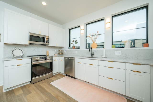 kitchen with tasteful backsplash, light wood-type flooring, a sink, white cabinets, and stainless steel appliances