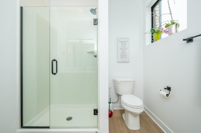 bathroom with toilet, baseboards, wood finished floors, and a stall shower