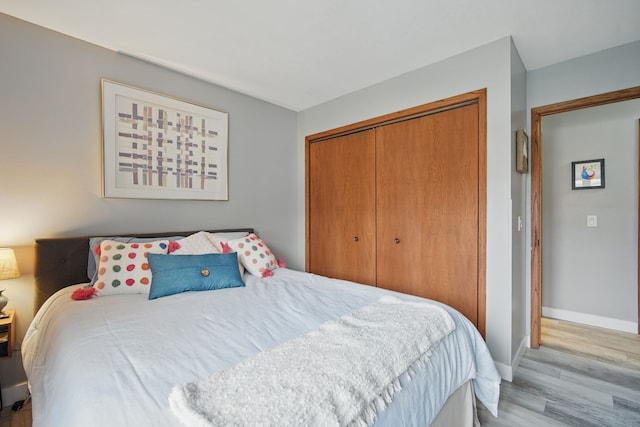 bedroom with a closet, light wood-style flooring, and baseboards