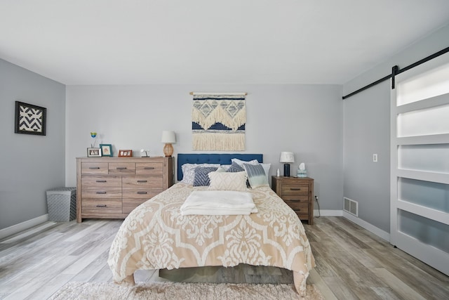 bedroom featuring visible vents, light wood-style flooring, a barn door, and baseboards
