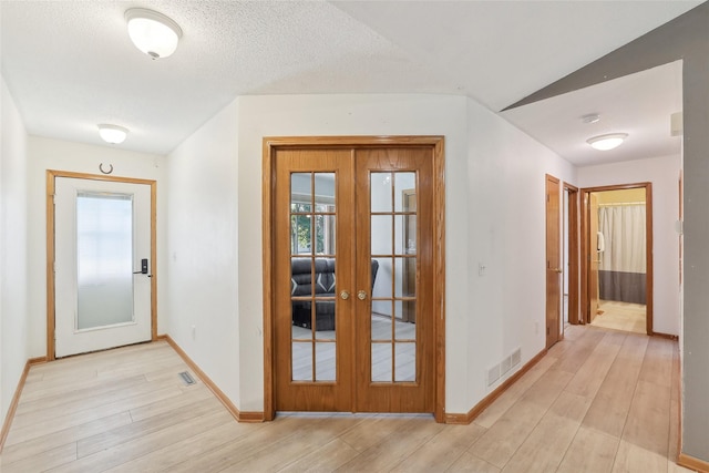 hallway with visible vents, light wood-style flooring, french doors, and baseboards