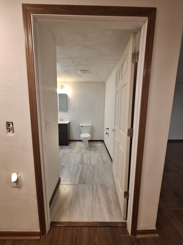 hall featuring a sink, a textured ceiling, and baseboards
