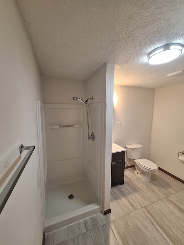 full bath featuring a textured ceiling, a stall shower, baseboards, toilet, and vanity