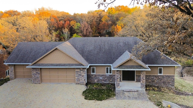 craftsman inspired home with driveway, stone siding, roof with shingles, a forest view, and a garage
