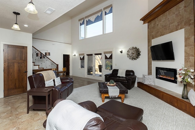 living area featuring stairway, a glass covered fireplace, a towering ceiling, and visible vents
