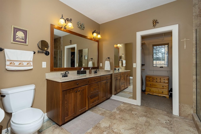 bathroom featuring a shower with door, toilet, double vanity, and a sink