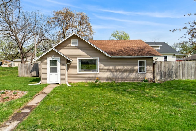 rear view of house featuring a yard, a shingled roof, and fence