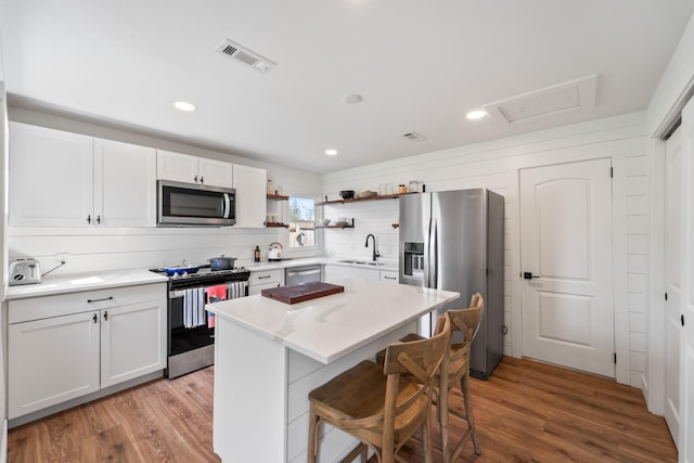 kitchen with a sink, stainless steel appliances, open shelves, visible vents, and light wood-style flooring