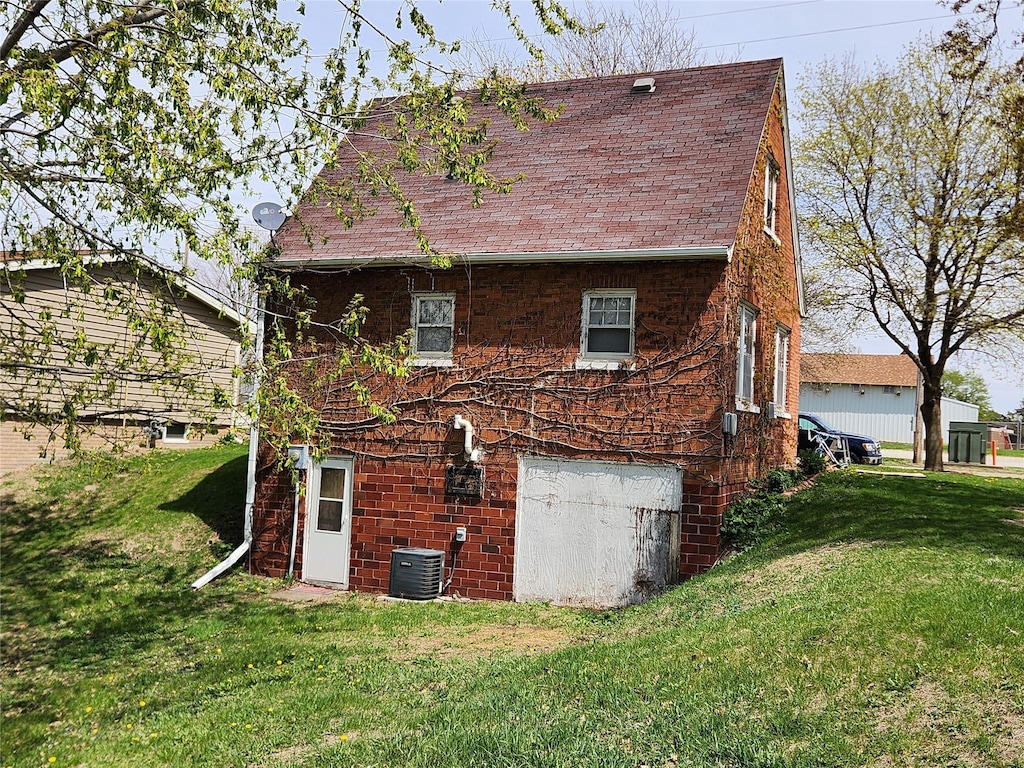 rear view of property with a yard, central AC unit, a shingled roof, and an attached garage