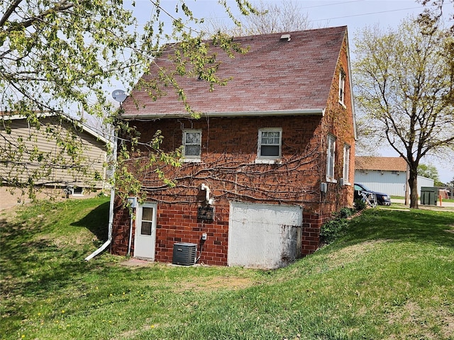 rear view of property with a yard, central AC unit, a shingled roof, and an attached garage