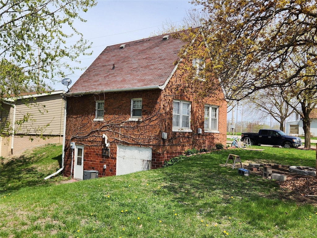 view of property exterior with a lawn, roof with shingles, central AC unit, and brick siding