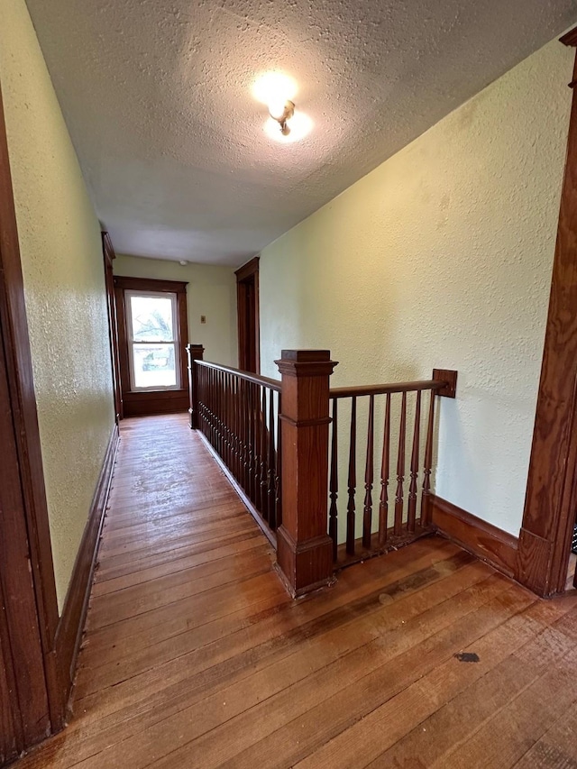 hall with an upstairs landing, a textured ceiling, a textured wall, and hardwood / wood-style flooring