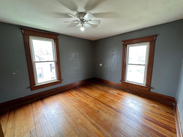 empty room featuring ceiling fan, a wealth of natural light, hardwood / wood-style flooring, and baseboards