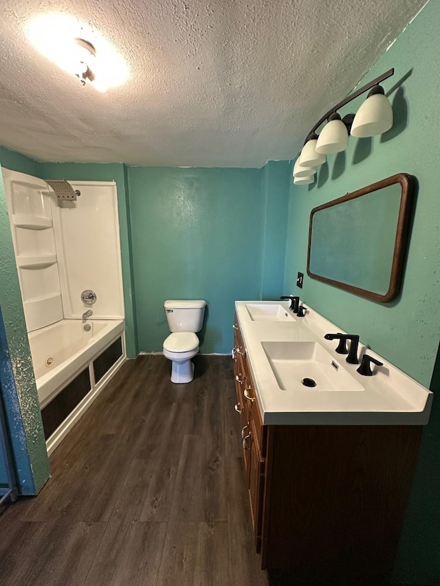 bathroom featuring wood finished floors, double vanity, toilet, a sink, and a textured ceiling