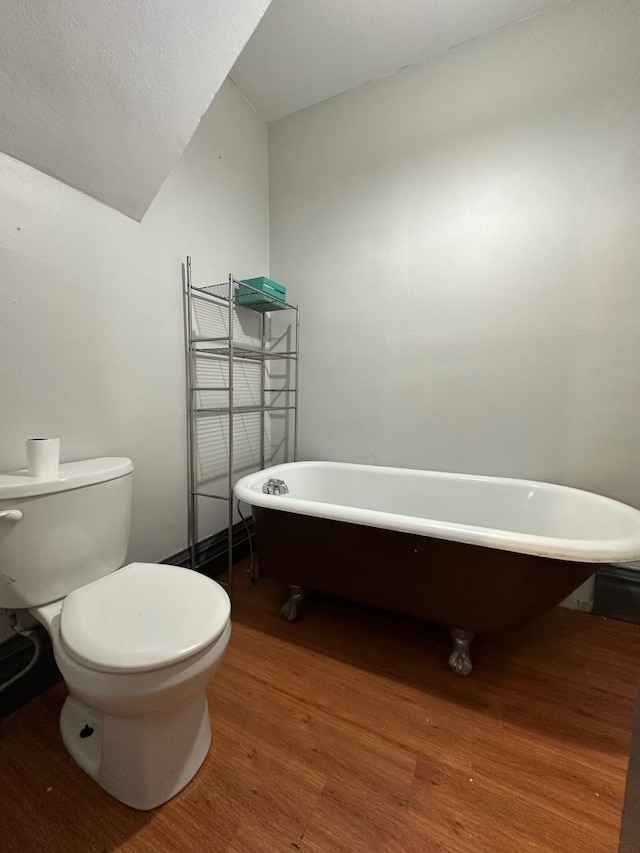 bathroom with toilet, wood finished floors, lofted ceiling, and a soaking tub