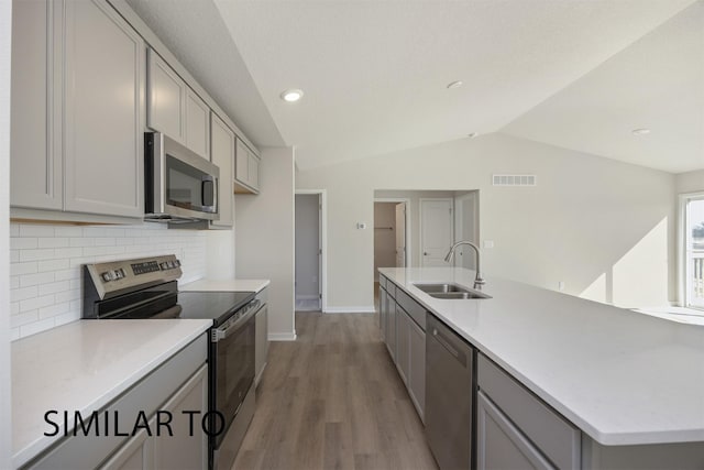 9394 Modena Ln, West Des Moines, IA 50266 - kitchen featuring stainless steel appliances, gray cabinets, vaulted ceiling, backsplash, and light wood-type flooring