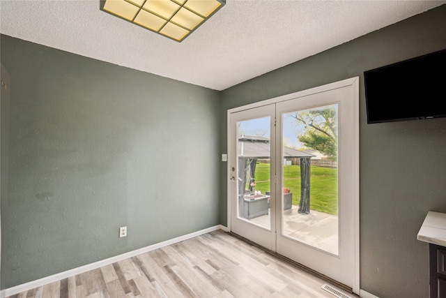 doorway featuring baseboards, a textured ceiling, and light wood-style flooring