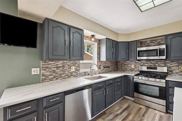 kitchen featuring a sink, tasteful backsplash, a textured ceiling, appliances with stainless steel finishes, and wood finished floors